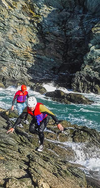 Two people scrambling up rocks on the Coasteering activity