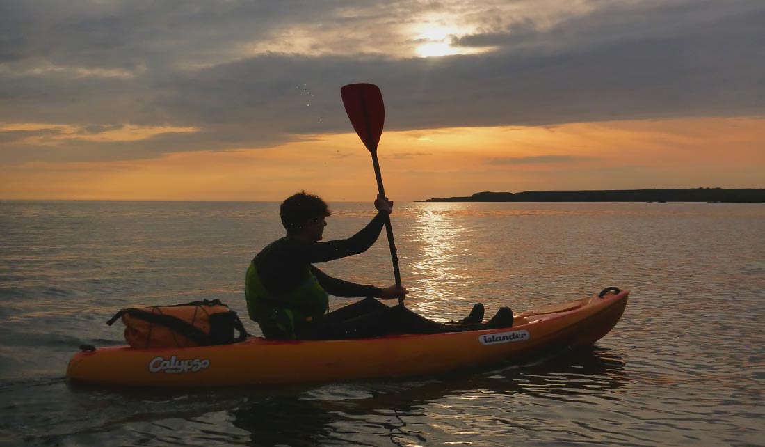 One man sea kayaking at sunset on Holy Island