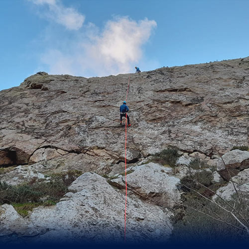 Man abseiling down a large cliff face as a guilde supports above